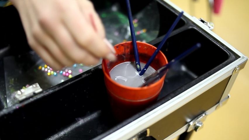 The artist washes his brushes in a plastic cup of water. Close-up cup with brushes for drawing. Tapping a brush on the edge of the cup.