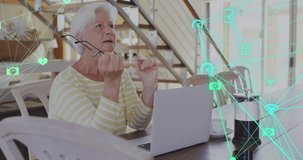 Animation of network of connections with icons over senior caucasian woman using laptop. global connections, digital interface and technology concept digitally generated video.