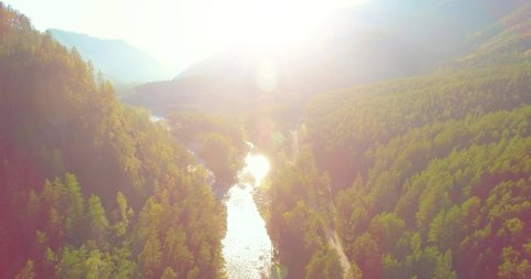 4K aerial point of view. Low altitude flight over fresh fast mountain river with rocks at sunny summer morning. Green pine trees and sun rays. Pure cold water stream.
