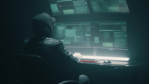 Hooded cybercriminal making cybercrime and hacking big data servers security system on computer in dark underground hideout
