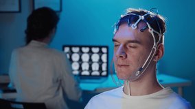 EEG topographer for examining brain, doctor making electrogram of scalp activity. Researching of brain work man wearing electroencephalography headset and watching video, nurse writing notes.