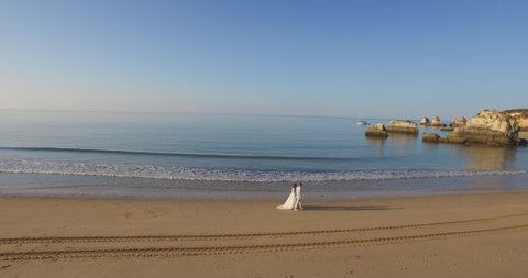 newlyweds walk along the ocean beach. Rocky coast. Portuguese beach. The bride is walking along the beach. sunny morning. Atlantic Ocean in Algarve