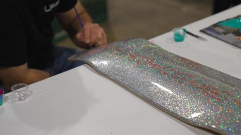 Los Angeles, CA USA - January 20 2022: This video shows the hand of an artist pin-striping and drawing on a metallic skate board.
