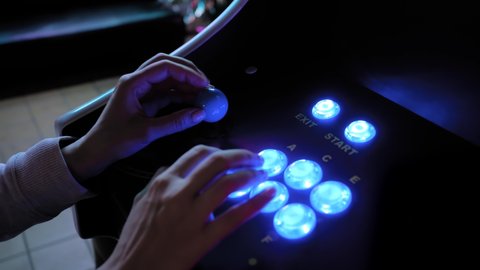 Woman hands playing retro arcade machine game and pushing bright colorful blue buttons in dark room - close up view. Gaming, 80s, hobby, vintage, technology, retro video game and leisure time concept