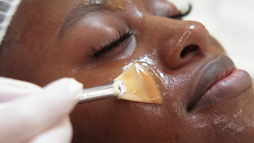 Moisturizing mask. Spa cosmetology. Facial rejuvenation. Closeup of cosmetologist hand applying cosmetic skincare product with brush on woman client face skin at salon. | Shutterstock HD Video #1087000532