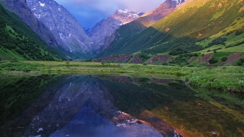 Beautiful landscape with high mountains with illuminated peaks, reflection in lake, sunlight of sunrise, 4k