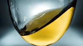 White wine splashing in a glass from side to side like waves. Glass with splashing wine close-up. Creative macro slow motion 4k video.