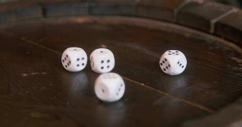 Pirate puts white marked cube-shaped dice on wooden barrel top to prepare for playing craps game IN cabin of ship close view