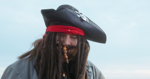 Crazy pirate captain in cocked hat with skull and crossbones and long braids rubs palms to fight ON beach near sea close view