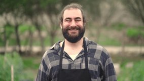 Slow motion video of bearded man with apron in garden smiling to camera