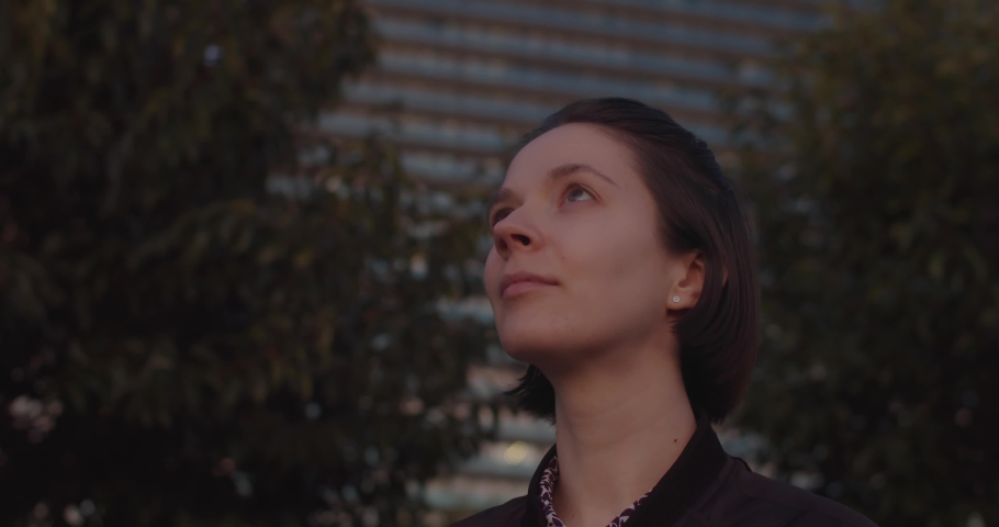 Profile portrait of young Caucasian woman looking up outdoors city park background copy space. Side view of attractive girl enjoying sunset sky view and smiling in evening. Freedom happiness success  | Shutterstock HD Video #1087010537