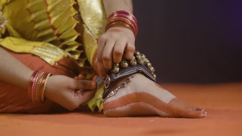 Rack focus shot, Bharatnatyam dancer removing music anklets or ghungroo khatak on stage after dancing - concept of classical dancer, Indian tradition and hobbyist