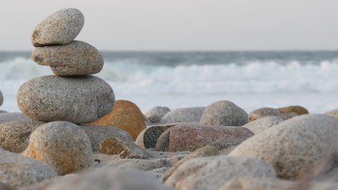 Rock balancing on pebble beach, Monterey 17-mile drive, California coast, USA. Stable pyramid stacks of round stones, sea ocean water waves crashing at sunset. Serenity harmony, calm zen meditation.