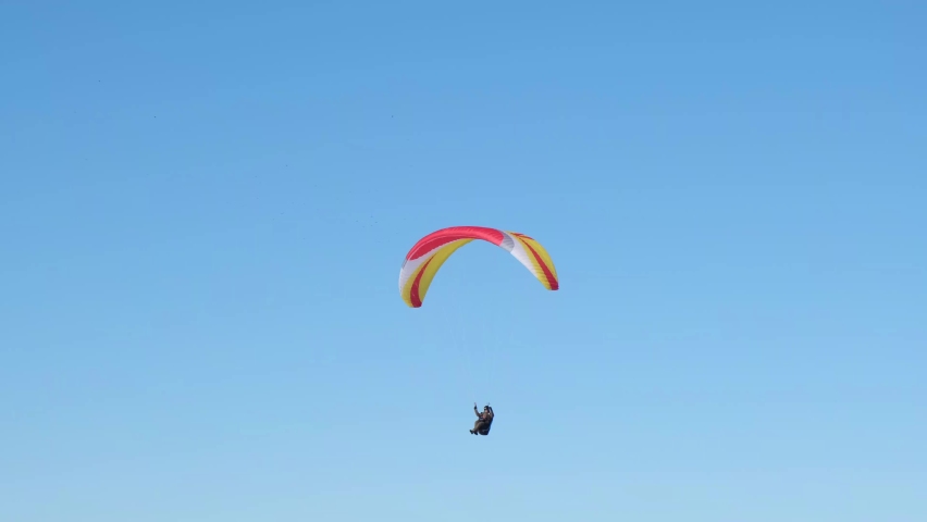 Paraglider soaring against the backdrop of a sunny blue sky. Bottom view