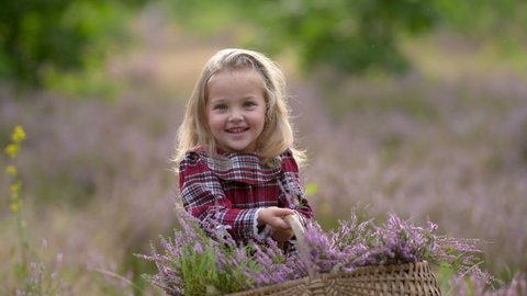 Cute little girl in a dress with a basket of wild flowers walks Outdoors in a green park. Happy Child Smiling outside. Summer vacation in nature. children, emotions.