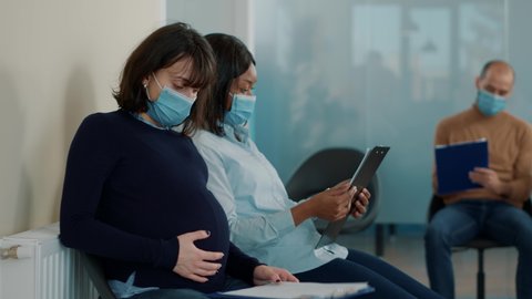 Woman expecting child and waiting to join executive job interview during pandemic. Pregnant applicant sitting in office lobby, reading cv files information and having career opportunity.