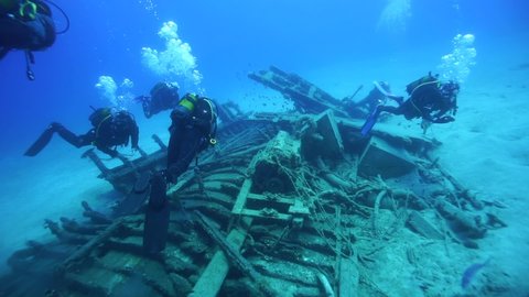 Six scuba divers explore the underwater wreck. Parrot fishes are in the ruined vessel wreck at the sandy bottom of the deep blue sea.