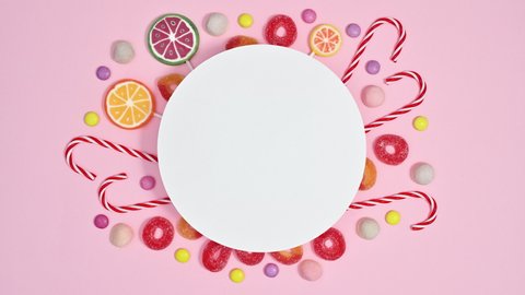 6k Sweets candies and lollipops appear under paper card note on pastel pink background. Stop motion flat lay