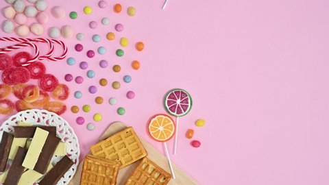 6k Sweet white and black chocolate and lollypops and candies appear on left side of pastel pink theme. Stop motion flat lay