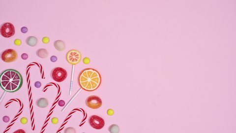 6k Pastel pink background with sweets candies and lollipops in left corner. Stop motion flat lay