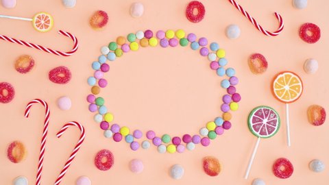 6k Candies and lollipops make creative frame copy space on bright pastel orange background. Stop motion flat lay
