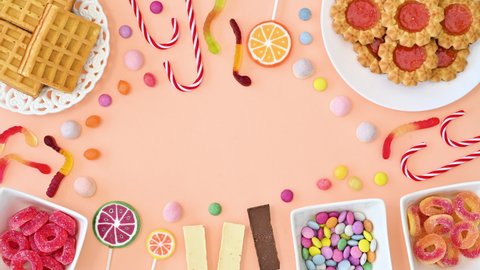 6k Creative frame copy space with sweet cookies, candies and lollipops on pastel bright orange backgorund. Stop motion flat lay