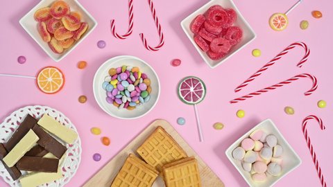 6k Sweet candies and lollypops and chocolates filling bowls on pastel pink theme. Stop motion flat lay animation