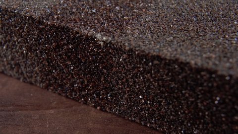 Sanding sponge block on wooden surface. Abrasive sandpaper rough texture. Macro. Rotation. Carpentry tool