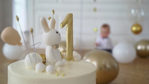 Celebration cake. Infant, small child. Baby boy dressed in suit - white shirt and bow tie. Childhood. Children is sitting on the floor. Birthday party or holiday celebration. White and yellow balloons