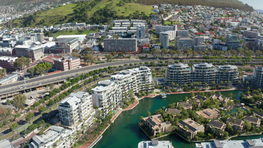 Drone footage slowly tracking sideways and looking down at the marina island and the buildings that surround it in Cape Town at high noon.