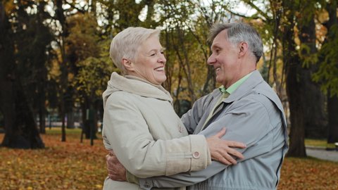 Joyful middle aged elderly couple hugging laughing standing in autumn park carefree chatting happy smiling grandma and grandpa embracing outdoors celebrating wedding anniversary family relationships