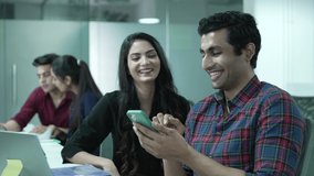 Two Indian friends, worker watching funny videos using smart phone laughing together. office Exterior.Indian male and female employee watching funny social media content while working office.