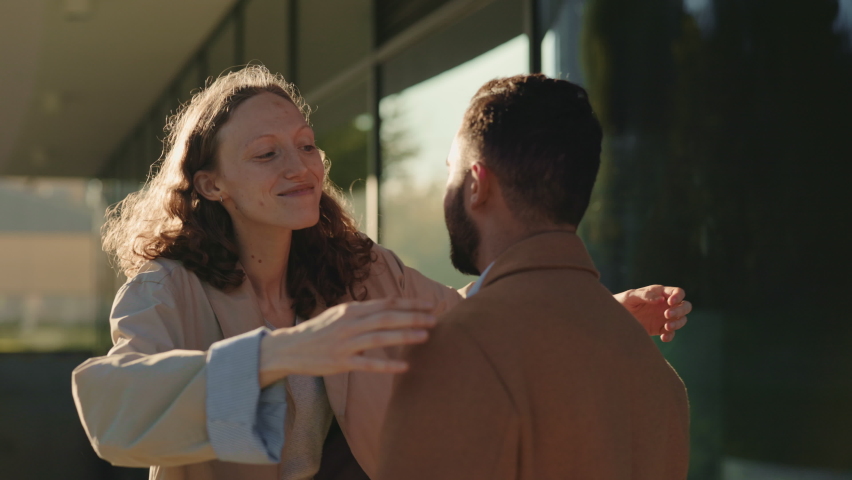 Happy young woman with curly hair embracing her loving dark haired man during meeting on street. Two loving people enjoying moments sending together.