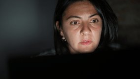 Woman face reading content online in front of computer screen at night