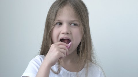 Child in white T-shirt brushing teeth with toothbrush on light background. Happy little girl brushing her teeth. Concept of children daily healthcare dental hygiene routine