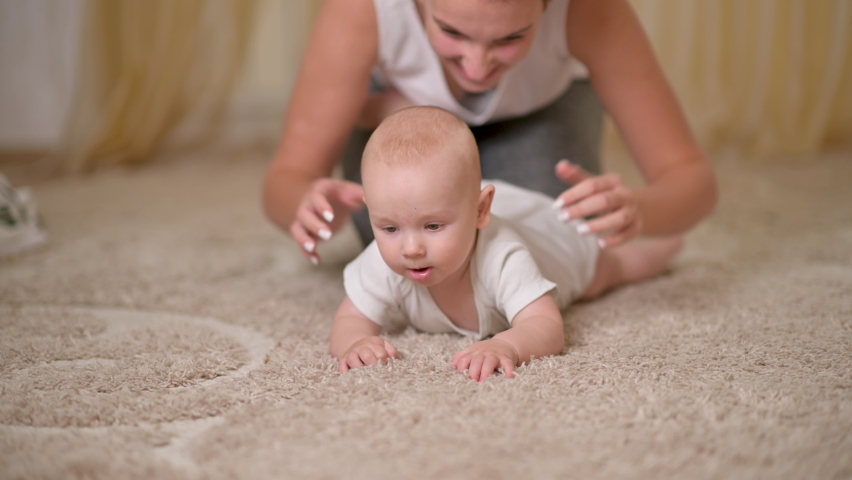 Loving tender young mum plays with adorable cute baby boy plays on the floor in the room. Mother and her new born baby girl at home. Concept of Childhood, Parenthood. beautiful happy family.