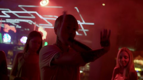 Group of young friends dances together in neon light of night club. Energetic playful moves in disco rhythm or hip-hop music. Partying joyful man at funky techno evening in bright multi-color shine