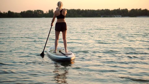 Girl Floating On Sup Board At Idyllic Evening. Swimming On Stand Up Paddle Board. Surfer Water Sports Active Lifestyle. Surfing On Inflatable SUP. Fun Rowing On Paddleboard Surfboard. Water Recreation