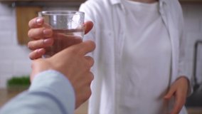 Girl holds out glass of water to man. Young woman is holding glass of water. Morning, hydration, skin care, beauty, diet food. Young family in home kitchen, starts new day with  healthy habit of life - Powered by Shutterstock - Get 15% off with code: PIKWIZARD15