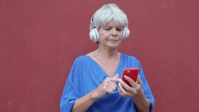 Senior woman using mobile smartphone listening and dancing to music playlist outdoor