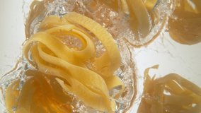 Super slow motion of falling uncooked italian pasta Tagliatelle into water, white background. Filmed on high speed cinema camera, 1000 fps. - Powered by Shutterstock - Get 15% off with code: PIKWIZARD15