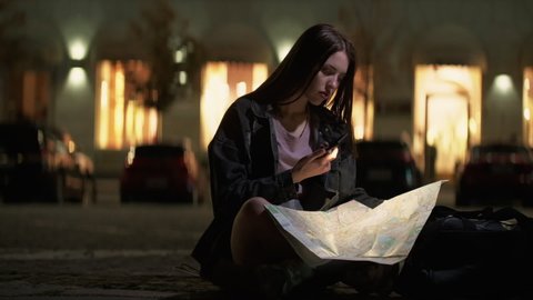 City explorer. Map reading. Trip direction. Pensive mindful young woman tourist searching travel destination way at late night street.