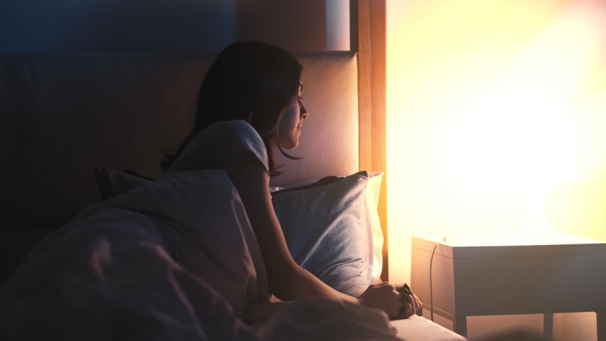 Sleep time. Healthy rest. Sweet dreams. Bedtime comfort. Peaceful relaxed young woman switching off lamp light switch in cozy soft bed after taking pill at late night dark bedroom.