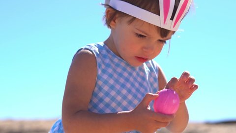 Close-up of Cute little girl wearing bunny ears holding Easter pink egg in hands. Happy Easter concept