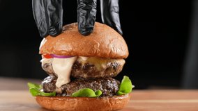 Hand putting top burger bun on a meat double cheeseburger with vegetables with sauce oozing and dripping out on black background. slow motion - Powered by Shutterstock - Get 15% off with code: PIKWIZARD15
