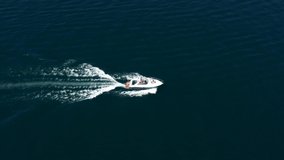 Flying over a white speed boat in motion. White big boat fast movement on dark blue water aerial view. High-speed motor boat with people moving on the water.