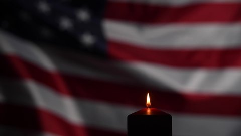 Burning candle against the background of the waving flag of the united states of america in the dark.