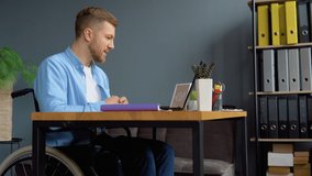 Cheerful disabled person talking on video chat while sitting at office in a wheelchair