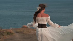 A young beautiful girl with dark hair, dressed in a white dress, is spinning on the top of the mountain, facing the wind blowing her hair and dress, and smiling - harmony, adventure, freedom, 4k video