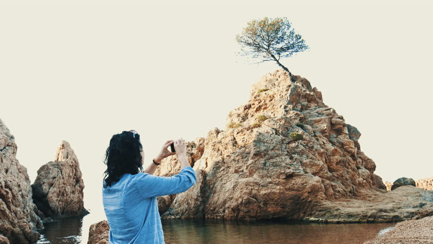 Dark curly hair woman takes a photo of the beach tree with her mobile phone